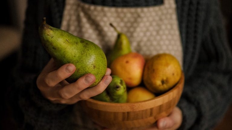 Close-up of hands holding a wooden bowl filled with fresh pears and other fruits, symbolizing healthy eating.