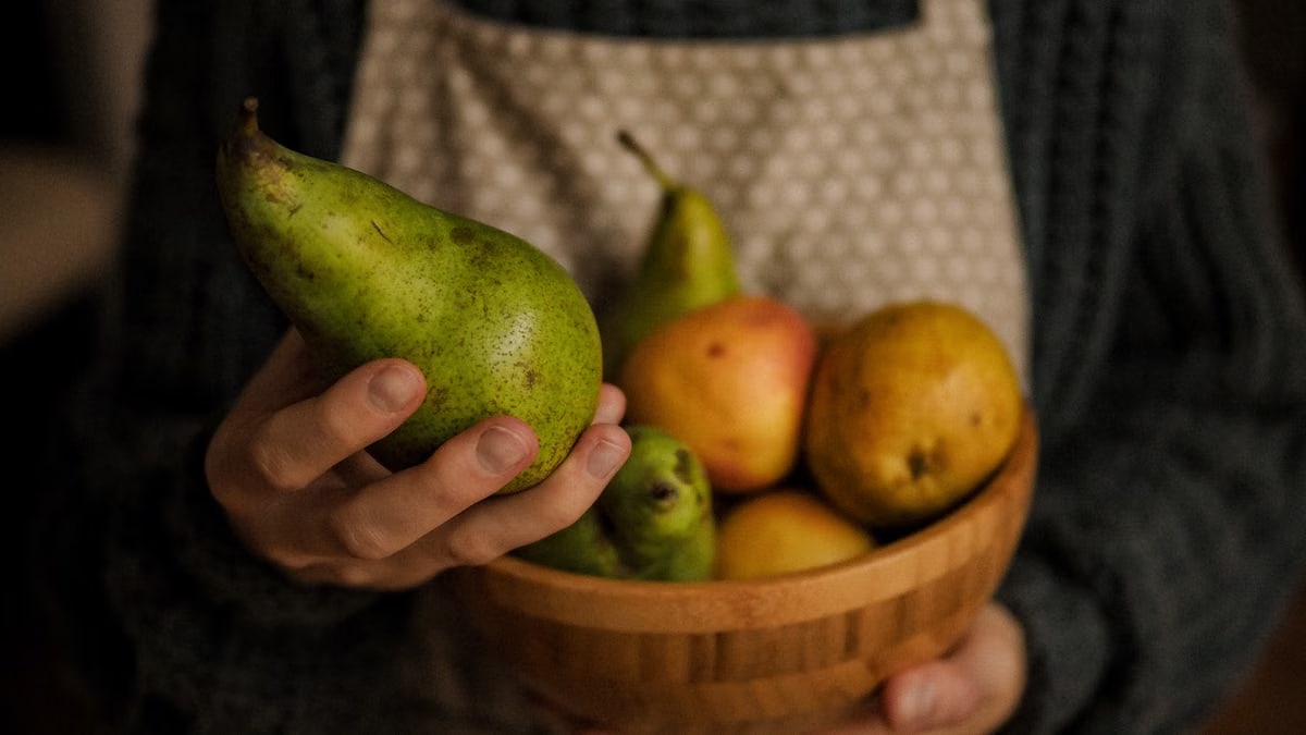 Close-up of hands holding a wooden bowl filled with fresh pears and other fruits, symbolizing healthy eating.